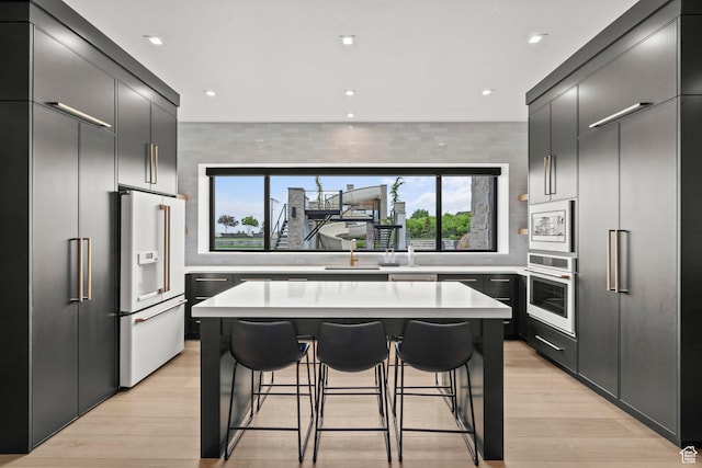 kitchen featuring white appliances, a breakfast bar, a kitchen island, light countertops, and decorative backsplash