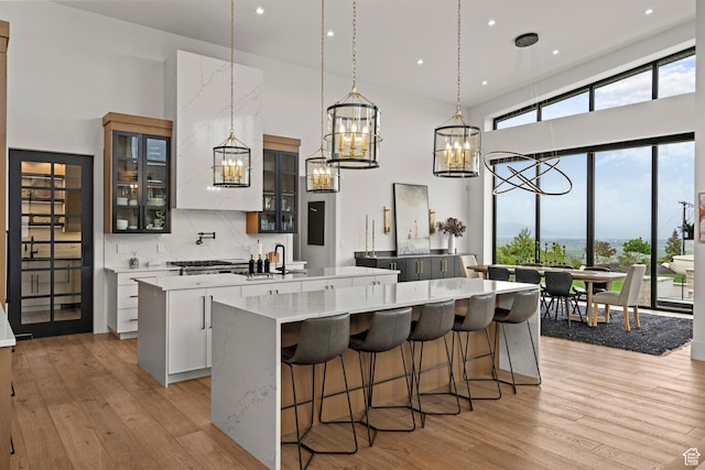 kitchen featuring a spacious island, a chandelier, a towering ceiling, light wood finished floors, and decorative light fixtures