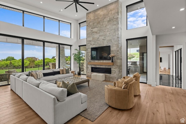 living room with a towering ceiling, ceiling fan, a fireplace, healthy amount of natural light, and hardwood / wood-style floors