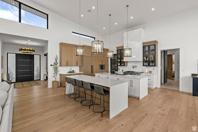 kitchen featuring a spacious island, high vaulted ceiling, a sink, backsplash, and light wood finished floors