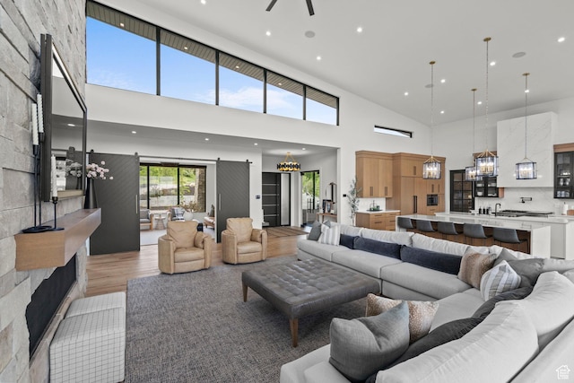 living area with a high ceiling, light wood-type flooring, recessed lighting, ceiling fan, and a chandelier