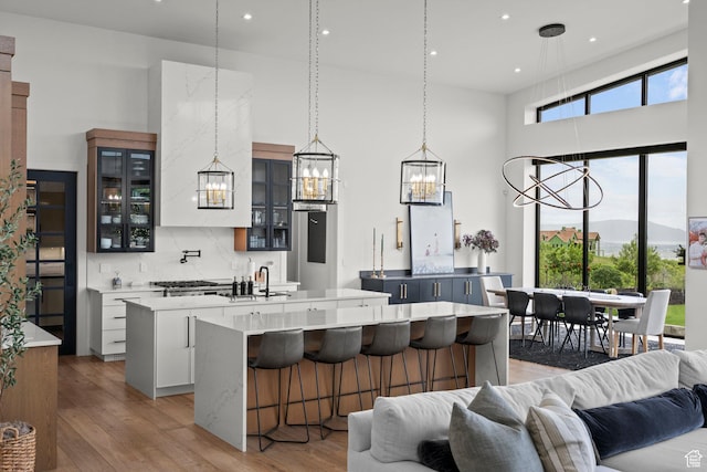 kitchen with an island with sink, a chandelier, open floor plan, light wood-style floors, and tasteful backsplash