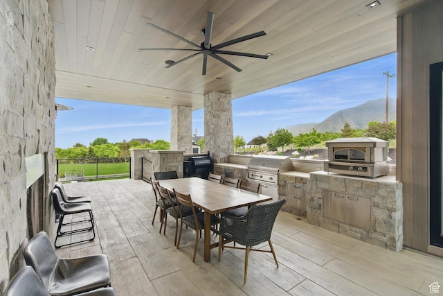 view of patio / terrace featuring exterior kitchen, grilling area, outdoor dining area, a ceiling fan, and a mountain view