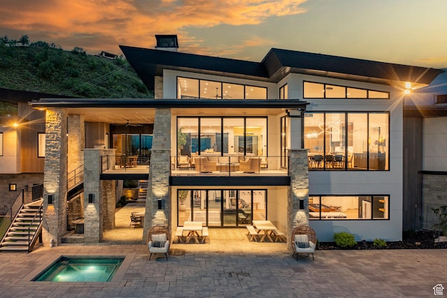 back of house at dusk featuring an in-ground hot tub, stairs, a patio, and a chimney