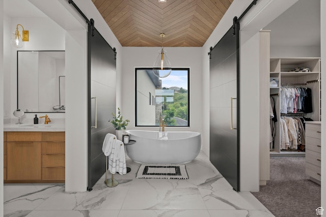 bathroom with vanity, a walk in closet, a freestanding tub, lofted ceiling, and marble finish flooring