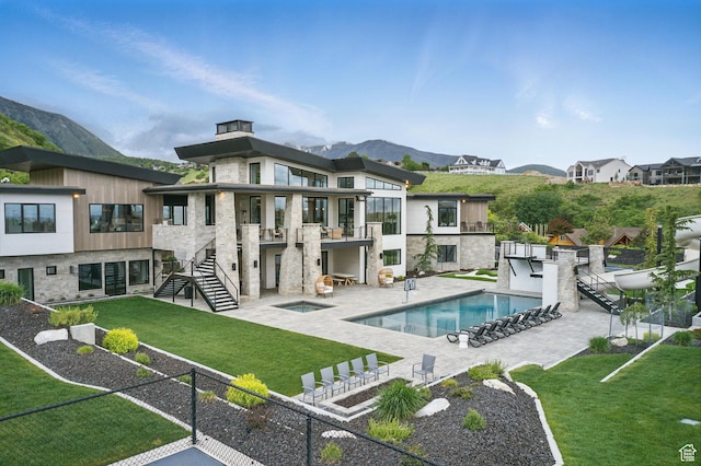 rear view of property featuring stairs, stone siding, a mountain view, an in-ground hot tub, and a patio area