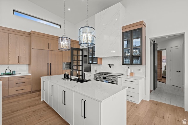 kitchen with high vaulted ceiling, a sink, a chandelier, appliances with stainless steel finishes, and glass insert cabinets