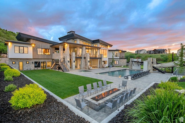 rear view of property featuring stairs, a fire pit, a yard, an outdoor pool, and stone siding