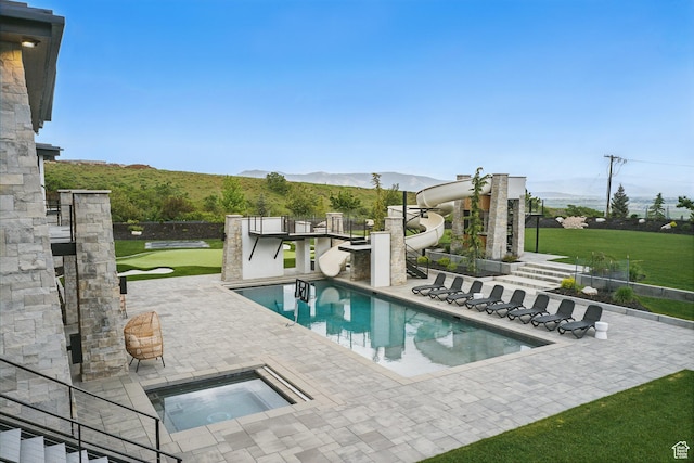 view of swimming pool with an in-ground hot tub, a water slide, a patio area, a mountain view, and a putting area