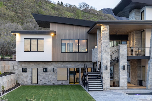 view of front facade with stone siding, a ceiling fan, a mountain view, a front lawn, and stairway