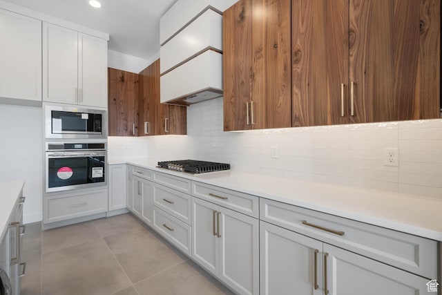 kitchen with stainless steel appliances, decorative backsplash, light countertops, light tile patterned floors, and white cabinets