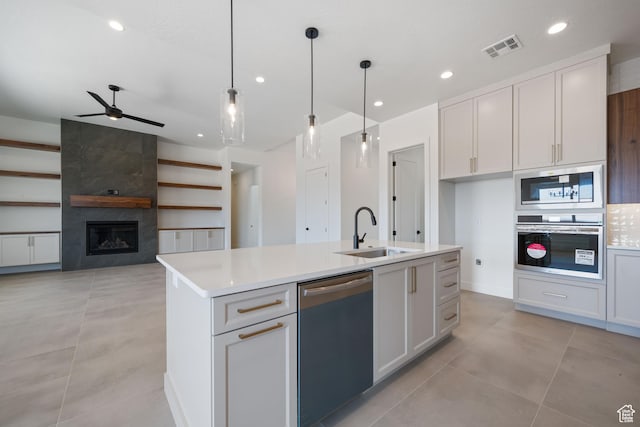 kitchen featuring a sink, appliances with stainless steel finishes, light countertops, ceiling fan, and a center island with sink