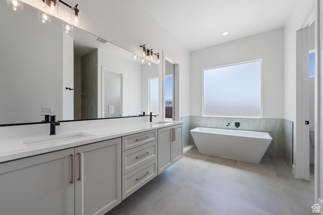 full bath featuring double vanity, tile walls, a soaking tub, a wainscoted wall, and tile patterned flooring