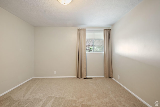 empty room with a textured ceiling, light colored carpet, and baseboards