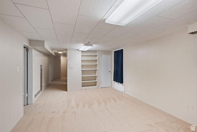finished basement with built in shelves, carpet floors, wood walls, and baseboards