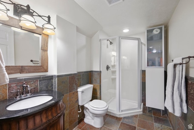 bathroom featuring toilet, a shower stall, vanity, tile walls, and stone tile flooring