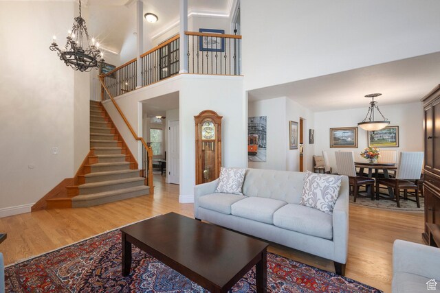 living area with light wood-type flooring, stairs, baseboards, a chandelier, and a towering ceiling