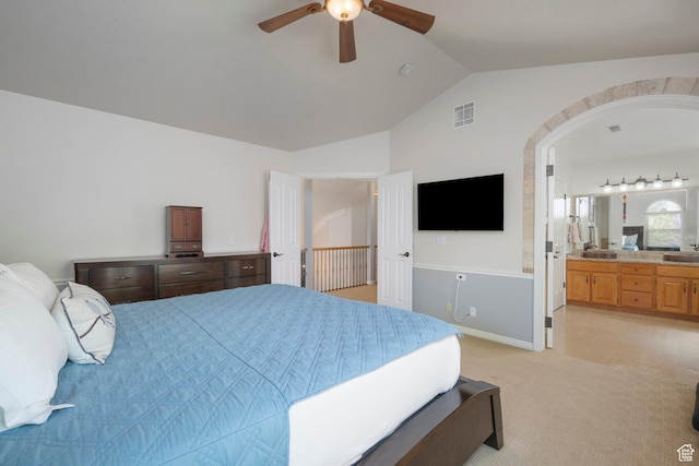 bedroom with lofted ceiling, arched walkways, light colored carpet, ensuite bathroom, and ceiling fan