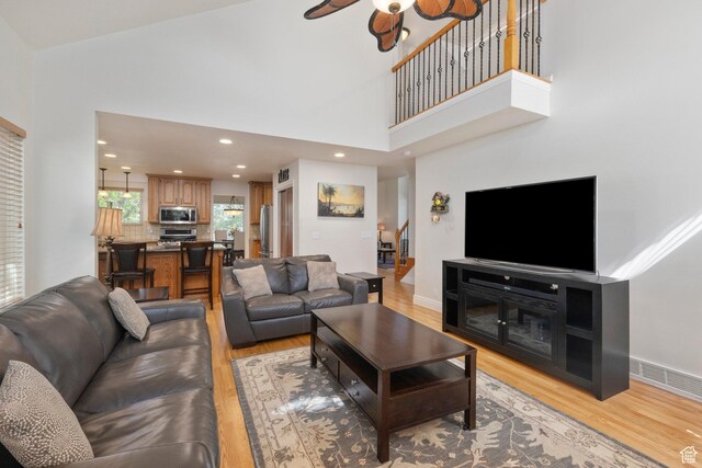living area featuring light wood-style flooring, a ceiling fan, a towering ceiling, baseboards, and recessed lighting