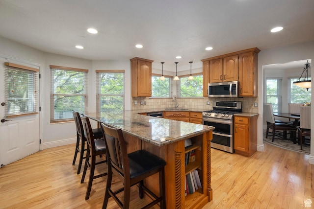 kitchen featuring appliances with stainless steel finishes, a sink, light wood-style floors, a breakfast bar, and recessed lighting
