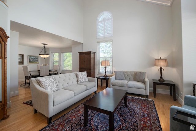 living room with a high ceiling, light wood-style floors, and baseboards
