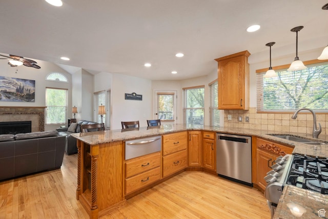 kitchen with dishwasher, a warming drawer, a sink, light stone countertops, and light wood-type flooring