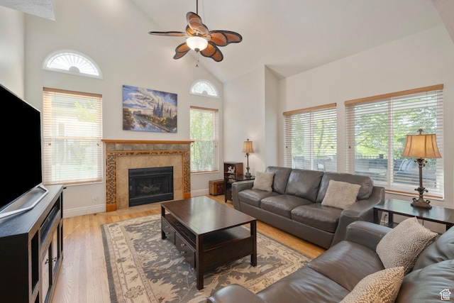 living room with plenty of natural light, high vaulted ceiling, a ceiling fan, light wood finished floors, and a tile fireplace