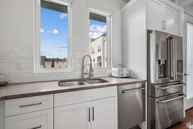 kitchen featuring appliances with stainless steel finishes, a sink, decorative backsplash, and white cabinetry