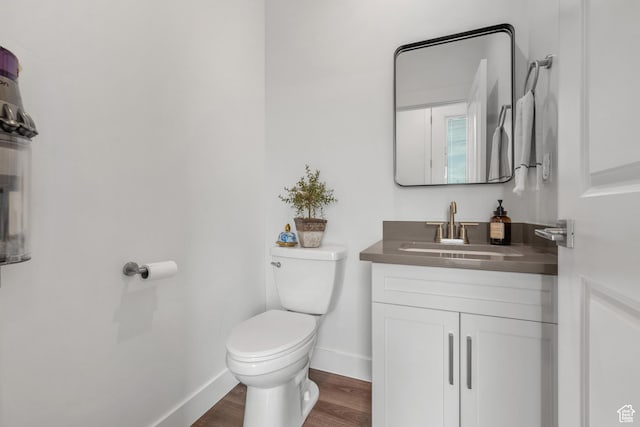 half bathroom featuring toilet, baseboards, wood finished floors, and vanity