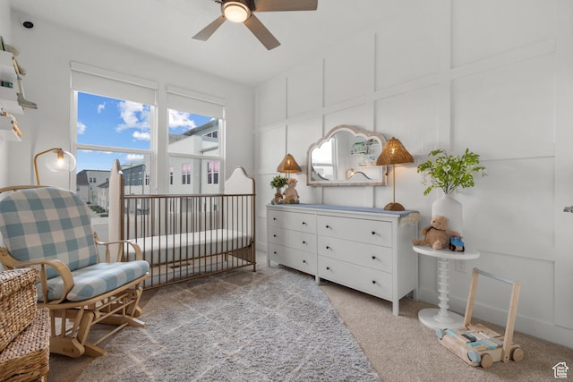 carpeted bedroom featuring a crib and a ceiling fan