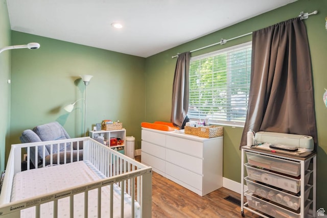 bedroom featuring wood finished floors, a crib, recessed lighting, and baseboards