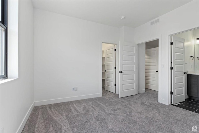 unfurnished bedroom with carpet flooring, baseboards, a walk in closet, and ensuite bath