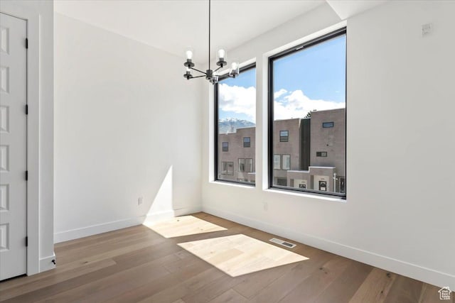 unfurnished dining area featuring baseboards, wood finished floors, and a chandelier