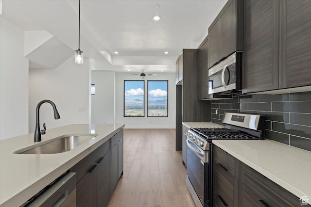 kitchen with stainless steel appliances, a sink, light wood-style floors, decorative backsplash, and light countertops