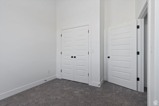 unfurnished bedroom featuring dark carpet, baseboards, and a closet