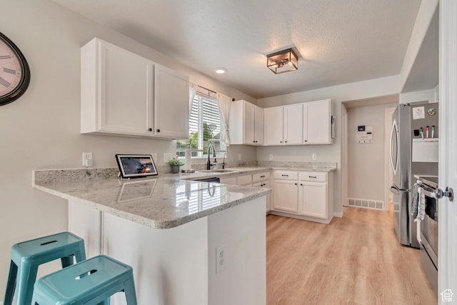 kitchen with a peninsula, appliances with stainless steel finishes, white cabinetry, light wood finished floors, and light stone counters