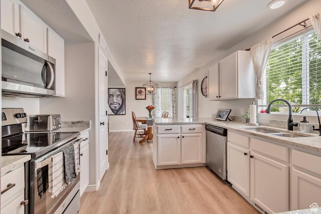 kitchen featuring appliances with stainless steel finishes, a sink, light wood-type flooring, a peninsula, and a chandelier