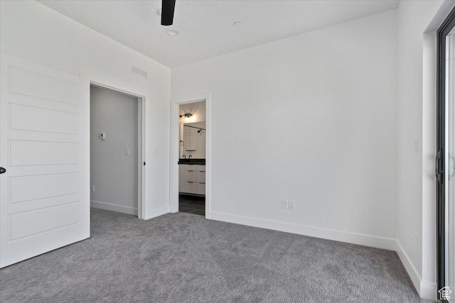 unfurnished bedroom with dark colored carpet, baseboards, and ensuite bath