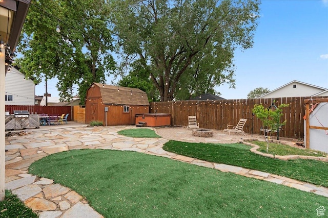 view of yard featuring a hot tub, an outdoor fire pit, a patio area, a storage shed, and an outbuilding