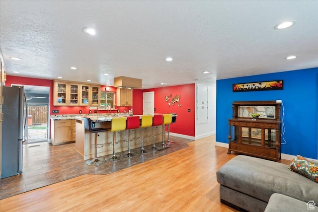 kitchen with freestanding refrigerator, light wood-style floors, a kitchen breakfast bar, recessed lighting, and glass insert cabinets
