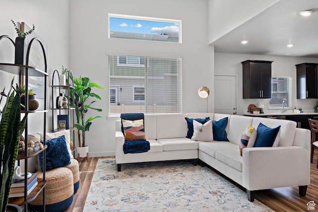 living room with light wood finished floors, plenty of natural light, a towering ceiling, recessed lighting, and baseboards