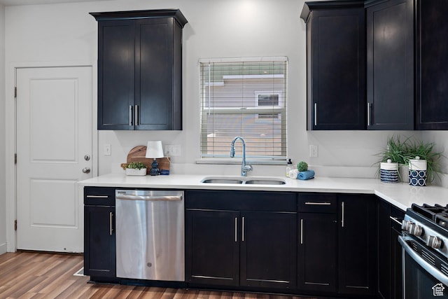 kitchen featuring stainless steel dishwasher, a sink, range with gas stovetop, and dark cabinets