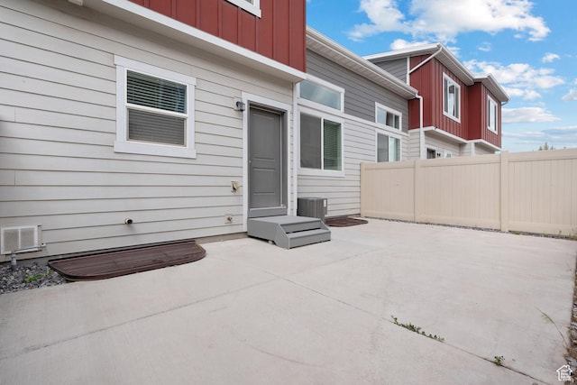 rear view of property featuring board and batten siding, fence, a patio, and cooling unit