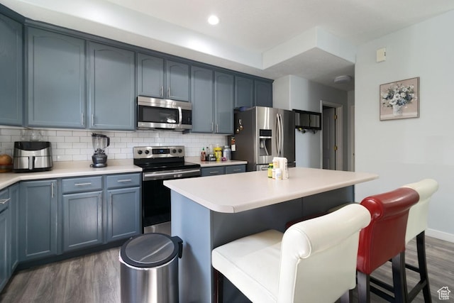 kitchen featuring appliances with stainless steel finishes, dark wood-style flooring, a kitchen breakfast bar, tasteful backsplash, and light countertops
