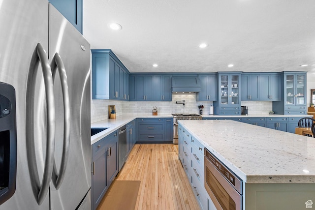 13956 S Wild Colt Cir, Herriman, UT 84096 - kitchen with appliances with stainless steel finishes, blue cabinets, backsplash, light wood finished floors, and a center island