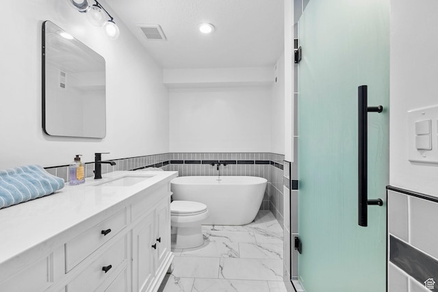13956 S Wild Colt Cir, Herriman, UT 84096 - bathroom featuring marble look tile flooring, a freestanding bath, wainscoting, vanity, and toilet