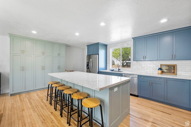 13956 S Wild Colt Cir, Herriman, UT 84096 - kitchen featuring appliances with stainless steel finishes, blue cabinets, a sink, a kitchen island, and light wood-type flooring