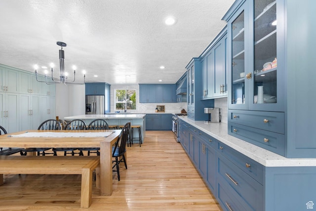 13956 S Wild Colt Cir, Herriman, UT 84096 - kitchen with appliances with stainless steel finishes, blue cabinets, custom range hood, a chandelier, and tasteful backsplash