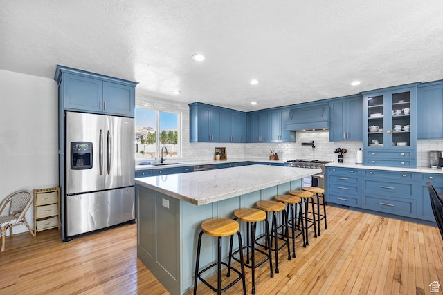 13956 S Wild Colt Cir, Herriman, UT 84096 - kitchen featuring appliances with stainless steel finishes, blue cabinetry, custom exhaust hood, light wood-type flooring, and a sink
