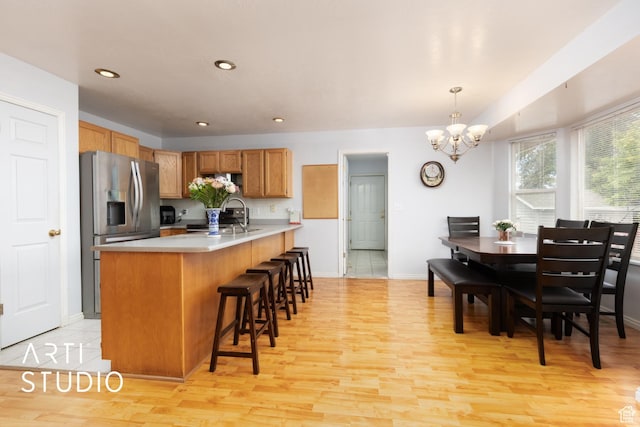 2956 W Mackay Meadows Pl, West Valley City, UT 84119 - kitchen with stainless steel refrigerator with ice dispenser, a chandelier, light countertops, light wood-style flooring, and a kitchen bar